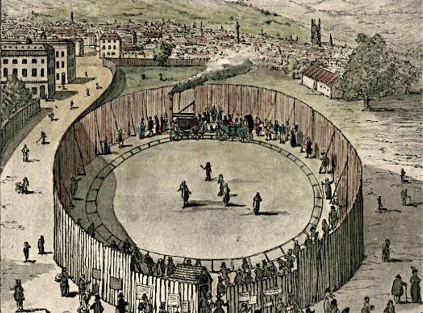 Primera parada: Dijon. El viaje inconcluso 3 A colored historical engraving of Richard Trevithick's "Steam Circus" in London, 1808. A high wooden fence forms a circular enclosure where the "Catch Me Who Can" steam locomotive pulls a carriage along a circular track. A crowd of people in period clothing watches the demonstration from outside the fence and inside the arena, with the cityscape of Bloomsbury and rolling hills visible in the background.