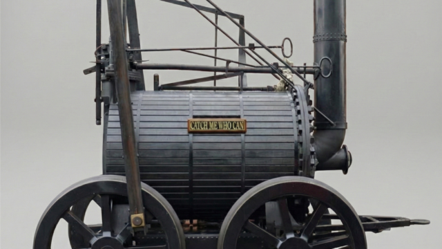 AI-generated 3D reconstruction of the Catch Me Who Can locomotive (1808). A realistic AI-generated 3D recreation of Richard Trevithick's "Catch Me Who Can" steam locomotive. The engine is depicted with a dark, metallic cylindrical boiler, large black spoked wheels, and a tall vertical smokestack. A small brass plaque on the side of the boiler reads "CATCH ME WHO CAN." The locomotive is presented against a neutral grey background, showcasing its complex system of rods and mechanical parts in high detail.