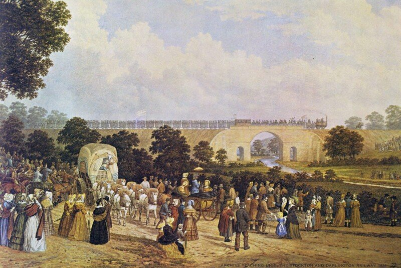 Tercera parada: Killingworth. ¡Vorwärts! 3 A 19th-century color lithograph depicting the opening of the Stockton and Darlington Railway in 1825. In the background, a long steam-powered train, led by the locomotive Locomotion No. 1, crosses a stone bridge over a river, with numerous passengers riding in open wagons. The foreground is filled with a large crowd of people in period attire—top hats, long coats, and bonnets—watching the spectacle. A horse-drawn carriage and a covered wagon are visible on a dirt road, illustrating the transition between traditional and modern transportation. The scene is set in a lush green landscape under a vast, pale sky.